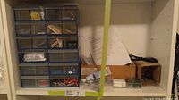 Full view of the plastic drawer organizer and adjacent cardboard boxes with additional items on shelf
