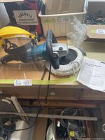 Full view of Makita electronic sander polisher with polishing pad, yellow protective face shield, and instruction manual on wooden surface.