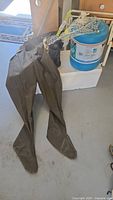 Pair of large Red Ball men's hip waders made of dark green/brown rubber with attached boots and a white fish net with metal frame resting on top of a medium sized Styrofoam cooler and a 20 liter Water Pak container.