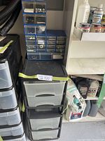 Stacking blue plastic organizer with small drawers holding nuts and bolts, sitting on top of black and clear plastic storage unit with four clear drawers.