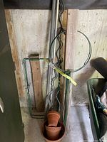 Garden stakes, poles, peony rings, clay pots, and bag holder in garden shed against wall