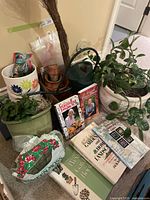 View of lot showing ceramic and clay pots, green metal watering can, live potted plant, bag of green moss, and gardening books.