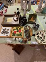 Photo showing various home decor pieces arranged on a table including framed art, small figurines, stained glass owl, polished stone bookends, carved wooden art, and miniature houses.
