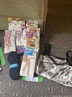 Photo showing multiple pairs of ladies hosiery, a Nine West floral camisole, and black felt cushion shoe insoles arranged on carpet