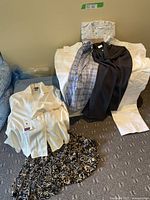Full lot photo showing white blouse with tags, blue plaid blouse, black blouse, beige slacks, and patterned skirt and pajama top