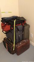 Stack of assorted luggage and bags including large suitcases, duffel bags, and hard case bag.