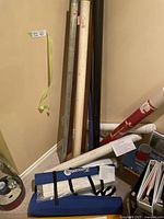 Various chart keeper roll-up tubes and fishing rod storage tubes in corner against wall, showing different materials, lengths, and colors.