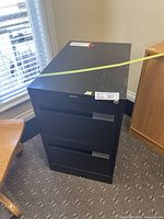 Black 2-drawer metal file cabinet closed, positioned on carpet.