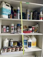 Shelf with various paint thinners, spray paints, solvents, and cleaners including Yamalube bottle, spray cans, and multiple small paint cans with labels