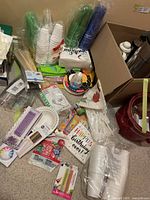 Image showing disposable plastic cups in different colors, paper plates, napkins with birthday themes, and assorted party accessories including straws and plastic cutlery.