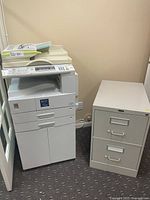 Photo showing Ricoh Aficio 2018D copier and Global 2-drawer file cabinet side by side in office space.
