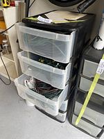 Three-tier plastic storage bin with transparent drawers holding multiple extension cords, black top.