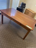 Full view of rectangular wooden dining table with drawer and brass feet