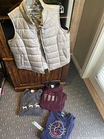 Three women's sweatshirts and one grey puffy vest displayed on floor and hanging on cabinet.