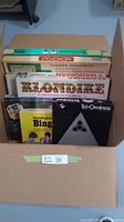 Image showing boxes of vintage board games neatly arranged inside a cardboard box including Klondike, Tri-Ominos, Waddingtons Bingo, Payday, and Monopoly.