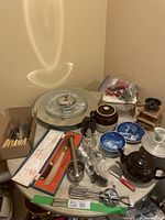 Overview photo showing various vintage kitchen items including ceramic pots, glass decanters, metal kitchen tools, blue and white plates, boxed carving set, and revolving cake stand