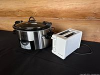 Crock-Pot programmable slow cooker and Proctor Silex 2-slice white toaster displayed side by side on black surface against wooden backdrop.