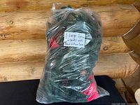 Three large artificial spruce garlands bundled inside a clear plastic bag with a paper label describing the contents.