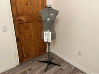 Full view of grey adjustable dress form on black tripod base in room setting