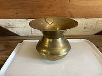 Front view of the antique brass spittoon showing wide-lipped opening, rounded base, and embossed shield.