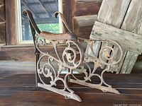 Side view showing one cast iron bench end with ornate Victorian scrollwork and shaped wooden armrest