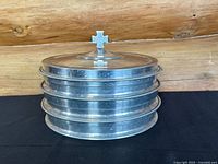 Three stacked aluminum trays with a domed lid topped by a raised cross finial, showing overall condition and construction.