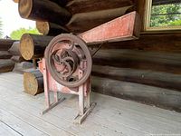 Front angle of the antique corn husker showing the feeder chute, large iron crank wheel, and wooden body with original faded red paint.