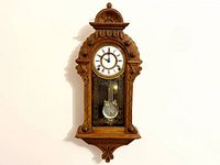 Full front view of the carved wood wall clock showing case shape, dial, and pendulum