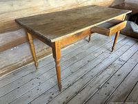 Large antique wood farmhouse table with a solid wood top and turned legs, single drawer open on side near one end, aged wood finish with marks and surface wear.