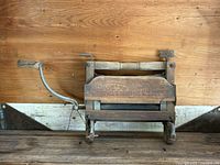 Full view of the antique wooden clothes wringer showing the wooden frame, hand crank on the left, and two rollers.