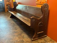 Photo showing the pew from the side with one end panel visible, displaying carved Gothic cross and trefoil decorations and the smooth contoured seat and backrest.
