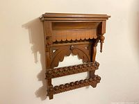 Front view of the antique Eastlake style wooden wall shelf with geometric and circular carved patterns, scalloped edges, and turned wood finials