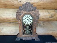 Full front view of antique Waterbury Clock Co. Dabney mantel clock showing carved oak case, clock dial, and pendulum visible through glass door.