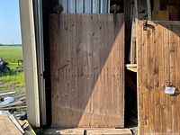 Front view of large antique wooden barn door showing weathered wood surface and original iron hardware at top.