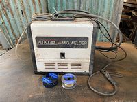 Front view of the Auto Arc MIG Welder with power/gun cables and two partial wire spools shown on the table.