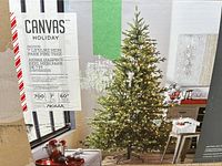 Photo of original cardboard box with product label showing image of tree and specifications including 7 feet height, 700 lights, 60 inch diameter, Canvas Holiday brand powered by NOMA.