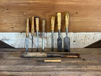 Front view of nine wood carving chisels with wooden handles arranged from narrow to wide blades and two additional larger gouges with rustic handles