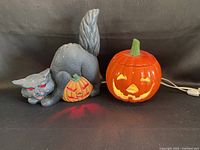 Full view of black cat Halloween figurine with red glowing eyes, small carved pumpkin, and ceramic jack-o’-lantern pumpkin light showing lighted eyes and mouth