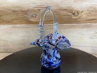 Full view of the hand-blown art glass basket showing ruffled edge and decorative clear handle with applied glass rings, set against a natural wood background.