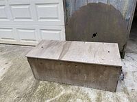 Wooden storage chest outdoors on concrete with a closed hinged lid showing its length and surface.