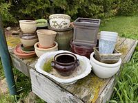 Photo showing multiple planters stacked and arranged on a weathered wooden table outdoors with greenery in the background.