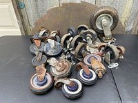 Top-down view of multiple vintage industrial swivel casters and wheels arranged on a black surface, showing range of sizes and types in lot.