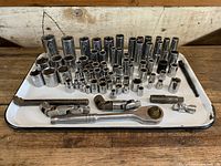 Full view of a white metal tray with an assortment of sockets and hand tools including ratchets, extensions, and universal joints