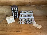 Wide view showing multiple rows of collectible thimbles displayed on a white riser and nearby collector cards on a wooden table with a wooden display shelf