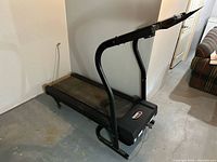 Side-angle view of used Leisure Works treadmill showing running belt, base, curved handles, and lower console area.