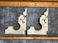 Front view of two antique architectural wood corbels with ornate scroll design and chippy white paint showing wear and patina.