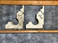 Front view of two antique wood corbels showing the ornate scroll design and chippy white paint.