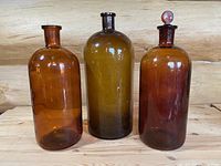Three large vintage apothecary bottles in amber and olive tones on a wooden surface against wood background.