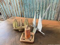 Photo showing all three vintage anchors arranged in a group on a metal surface against a corrugated blue wall background