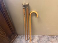 Full view of three walking sticks, two with brass handles and tips, one with curved wood handle